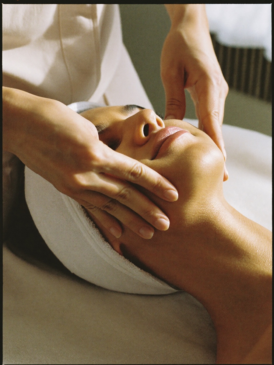 A facialist's hands sculpting a client's jawline and cheek during a buccal face lift