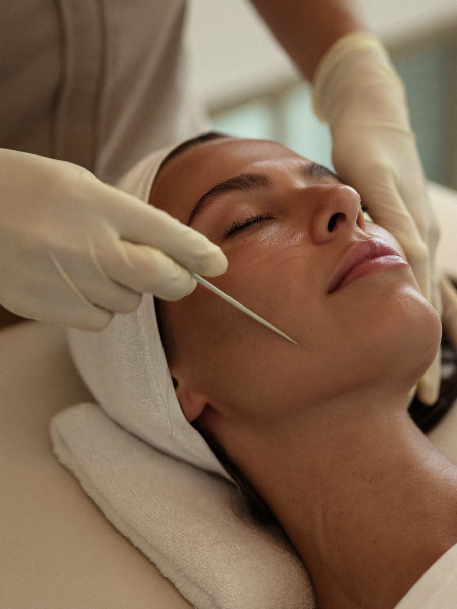 A gloved facialist holding a dermaplaning blade flat against a client's cheek