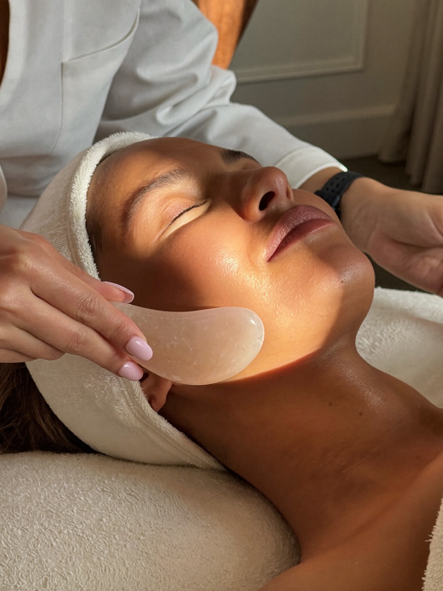 A hand-carved rose quartz gua sha stone gliding along a client's jawline
